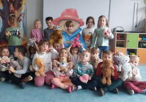 Dzieci pozują do wspólnego zdjęcia prezentując ulubione przytulanki - pluszowe misie.