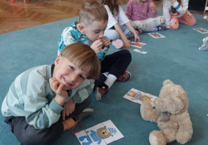 Dzieci siedzą na dywanie. Przed dziećmi leżą układanki z misiami.