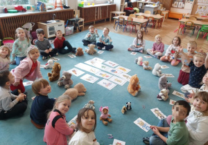 Dzieci siedzą na dywanie. Przed dziećmi leżą układanki z misiami. Ujęcie na całą grupę.