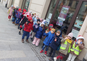 Grupa dzieci pozuje do wspólnego zdjęcia stojąc przed witryną sklepową w Łodzi.