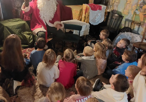 Dzieci siedzą przed Mikołajem i z zaciekawieniem przysłuchują się opowieści.