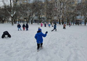 Grupa dzieci w zimowych strojach biega i bawi się w pełnym śniegu ogrodzie w przedszkolu. Ujęcie 1
