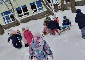 Grupa dzieci w zimowych strojach biega i bawi się w pełnym śniegu ogrodzie w przedszkolu. Ujęcie 2