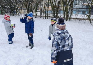 Grupa dzieci w zimowych strojach biega i bawi się w pełnym śniegu ogrodzie w przedszkolu. Ujęcie 1