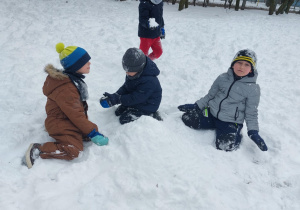 Grupa dzieci w zimowych strojach biega i bawi się w pełnym śniegu ogrodzie w przedszkolu. Ujęcie 3