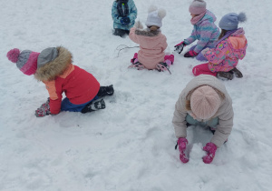 Grupa dzieci w zimowych strojach biega i bawi się w pełnym śniegu ogrodzie w przedszkolu. Ujęcie 6