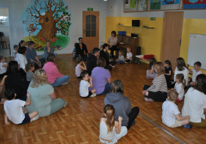 Rodzice i dzieci siedzą w parach. Dzieci rysują paluszkami na plecach rodziców.