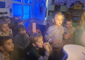 Grupa dzieci przygląda się źródłu światła poza kadrem.