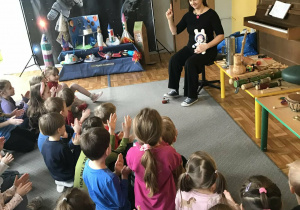 Nauczycielka siedzi na krzesełku i opowiada dzieciom o instrumentach i muzyce.