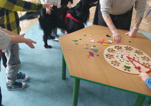 Dzieci i nauczycielka układają w grze "loteryjce" kształt psiej łapy.