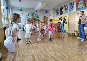 Dzieci i nauczycielki w czasie zajęć ruchowych wykonują ćwiczenia gimnastyczne - kręcenie biodrami.
