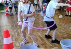 Dzieci w czasie zajęć ruchowych wykonują zadanie wspólnie przechodząc przez kółko gimnastyczne.