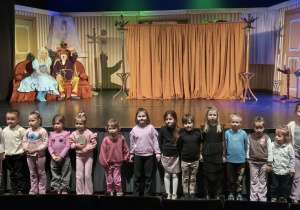 Dzieci pozują do wspólnego zdjęcia na tle sceny i aktorów. Grupa 5