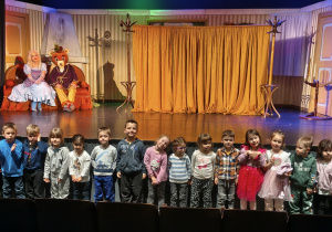 Dzieci pozują do wspólnego zdjęcia na tle sceny i aktorów. Grupa 2