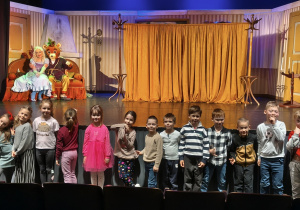 Dzieci pozują do wspólnego zdjęcia na tle sceny i aktorów. Grupa 4