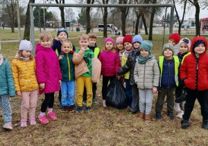 Dzieci pozują do wspólnego zdjęcia w czasie sporzątania terenów zielonych wokół przedszkola. Grupa 4