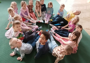 Dzieci w kolorowych skarpetkach siedzą na dywanie w ciasnym kółeczku. Grupa 2