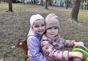 Dzieci z grupy 1 bawią się w ogrodzie przedszkolnym wczesną wiosną. Ujęcie 1. Dwoje dzieci siedzi na bujaczku.