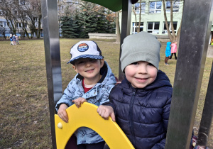 Dzieci z grupy 1 bawią się w ogrodzie przedszkolnym wczesną wiosną. Ujęcie 4. Dwoje dzieci uśmiecha się w czasie zabawy na ogrodowej zjeżdżalni.