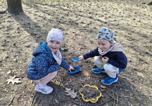 Dzieci z grupy 1 bawią się w ogrodzie przedszkolnym wczesną wiosną. Ujęcie 6. Dwoje dzieci zbiera patyczki.