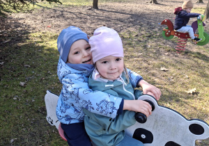 Dzieci z grupy 1 bawią się w ogrodzie przedszkolnym wczesną wiosną. Ujęcie 7. Dwoje dzieci siedzi razem na bujaczku.