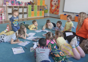 Dzieci i nauczycielka siedzą na dywanie. Dzieci przeglądają kolorowe książeczki. Grupa 3