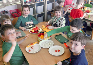 Dzieci z grupy 3 siedzą przy stoliku i przygotowują owoce do "owocowych szaszłyków". Ujęcie 1