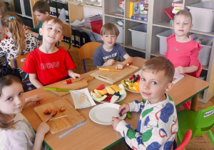 Dzieci z grupy 3 siedzą przy stoliku i przygotowują owoce do "owocowych szaszłyków". Ujęcie 2