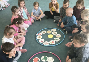 Dzieci siedzą na dywanie, a pomiędzy nimi znajdują się obrazki z żywnością. Ujęcie 1