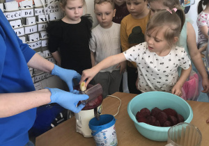 Dzieci i nauczycielka wspólnie wykonują soki korzystając z sokowirówki.