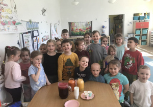 Cała grupa pozuje do wspólnego zdjęcia po zakończeniu zajęć. Przed dziećmi na stoliku znajdują się wykonane soki.