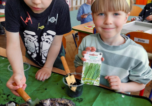 Dwoje dzieci przy stoliku wysiewa nasiona do pojemników.