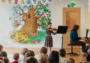 Dziecko gra na instrumencie. Widać dzieci siedzące na scenie. Ujęcie 2