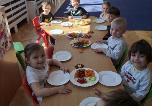 Grupa dzieci siedzi przy stole zastawionym warzywami i owocami. Ujęcie 3
